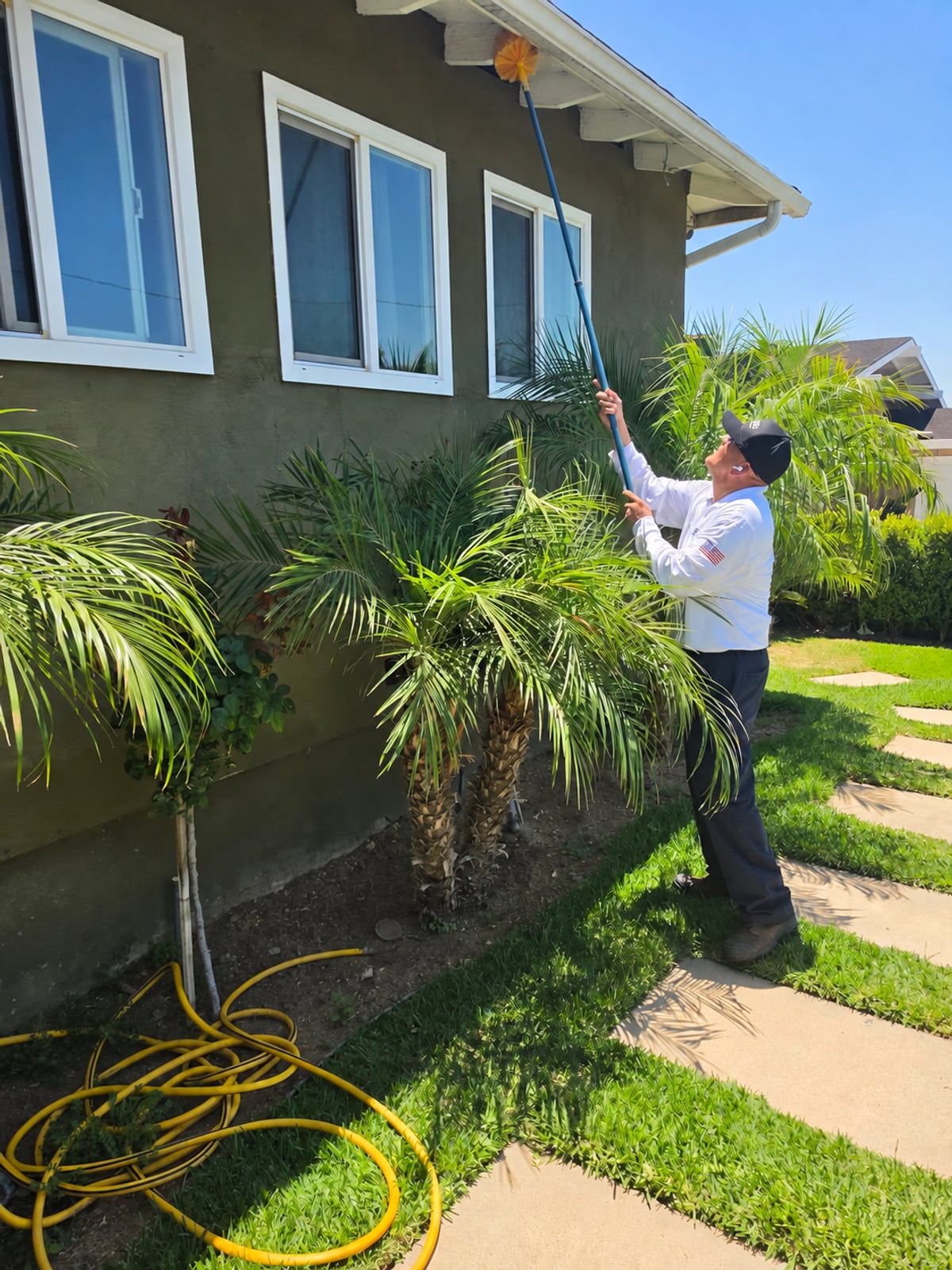 Raul removing spider webs from exterior eaves during pest service at a La Habra home